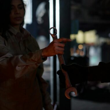 A mechanic handing over a wrench in a dimly lit garage workshop, creating a moody atmosphere.