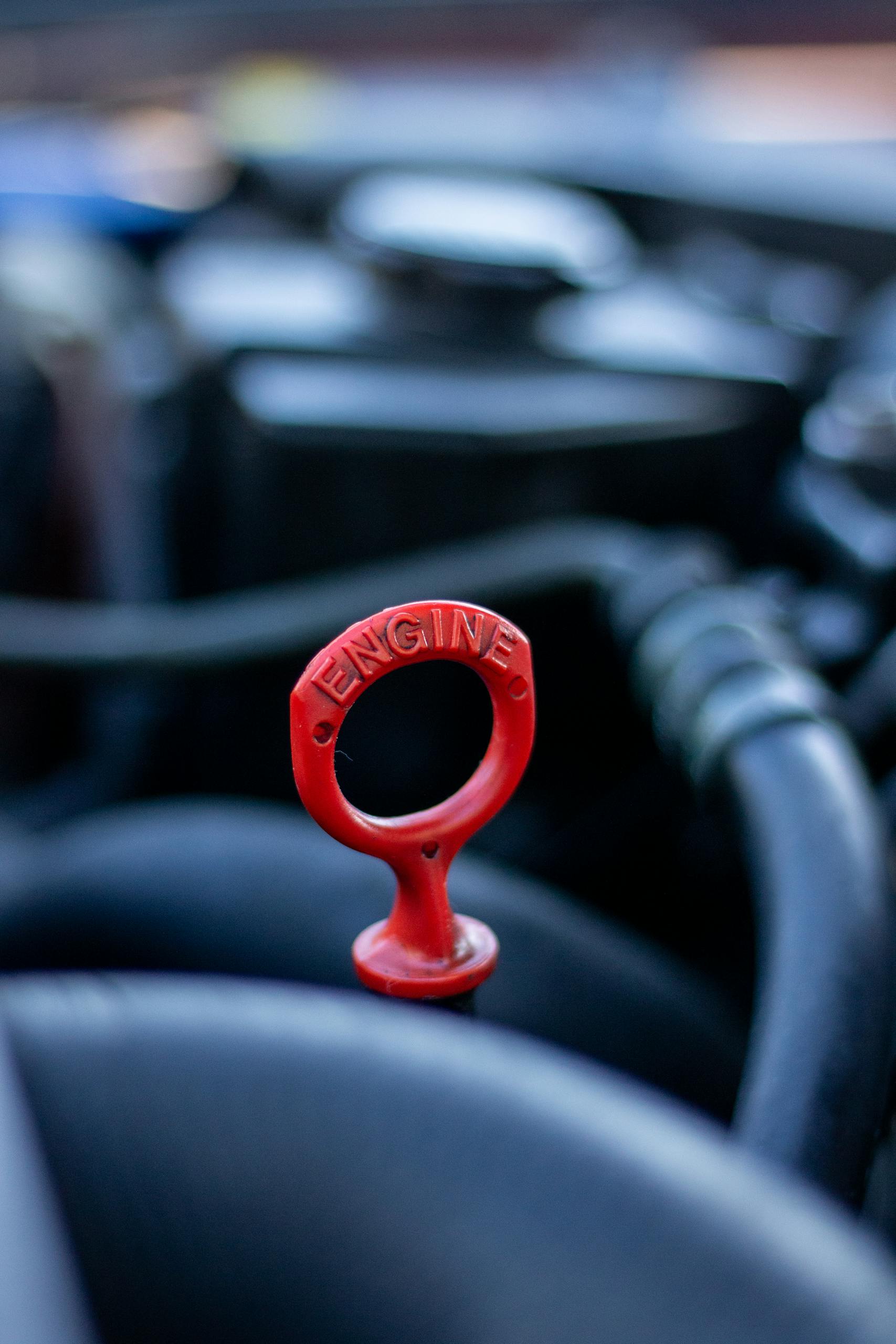 Detailed view of a red engine dipstick in an automobile, emphasizing selective focus and automotive mechanics.